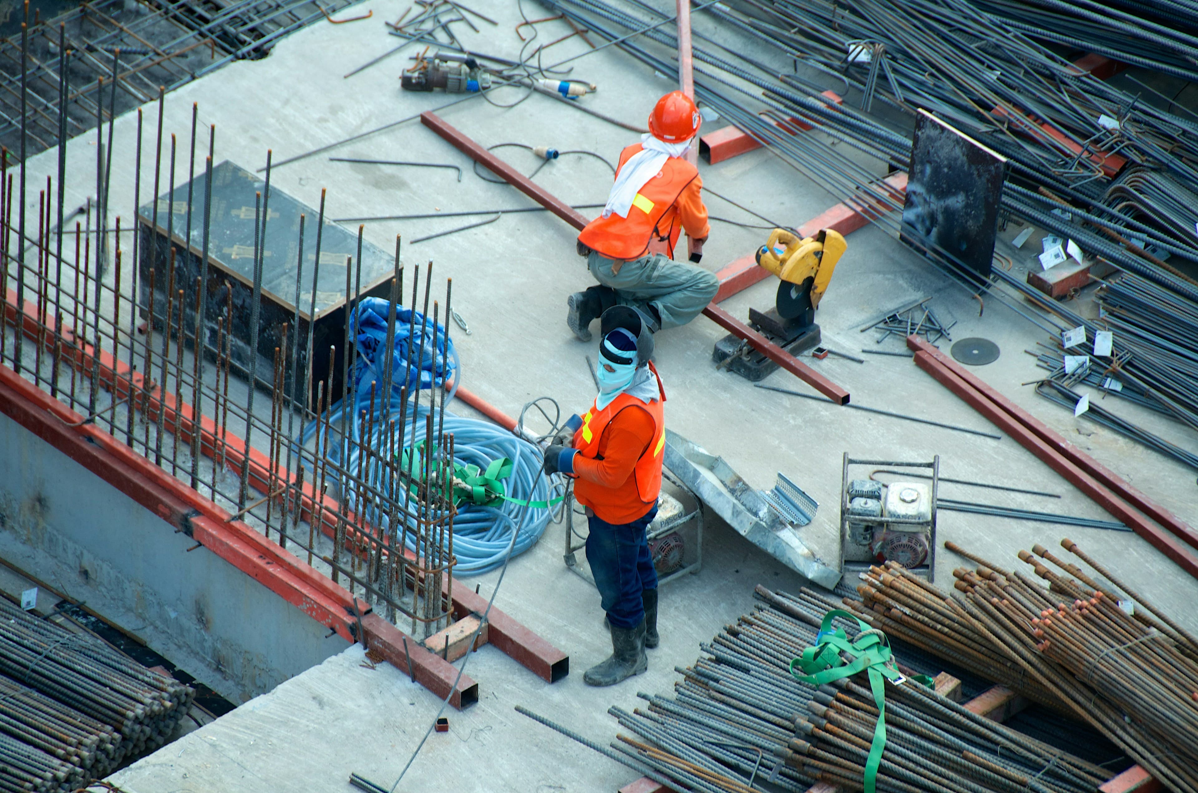 Two construction workers on a building site among steel, formwork, and concrete