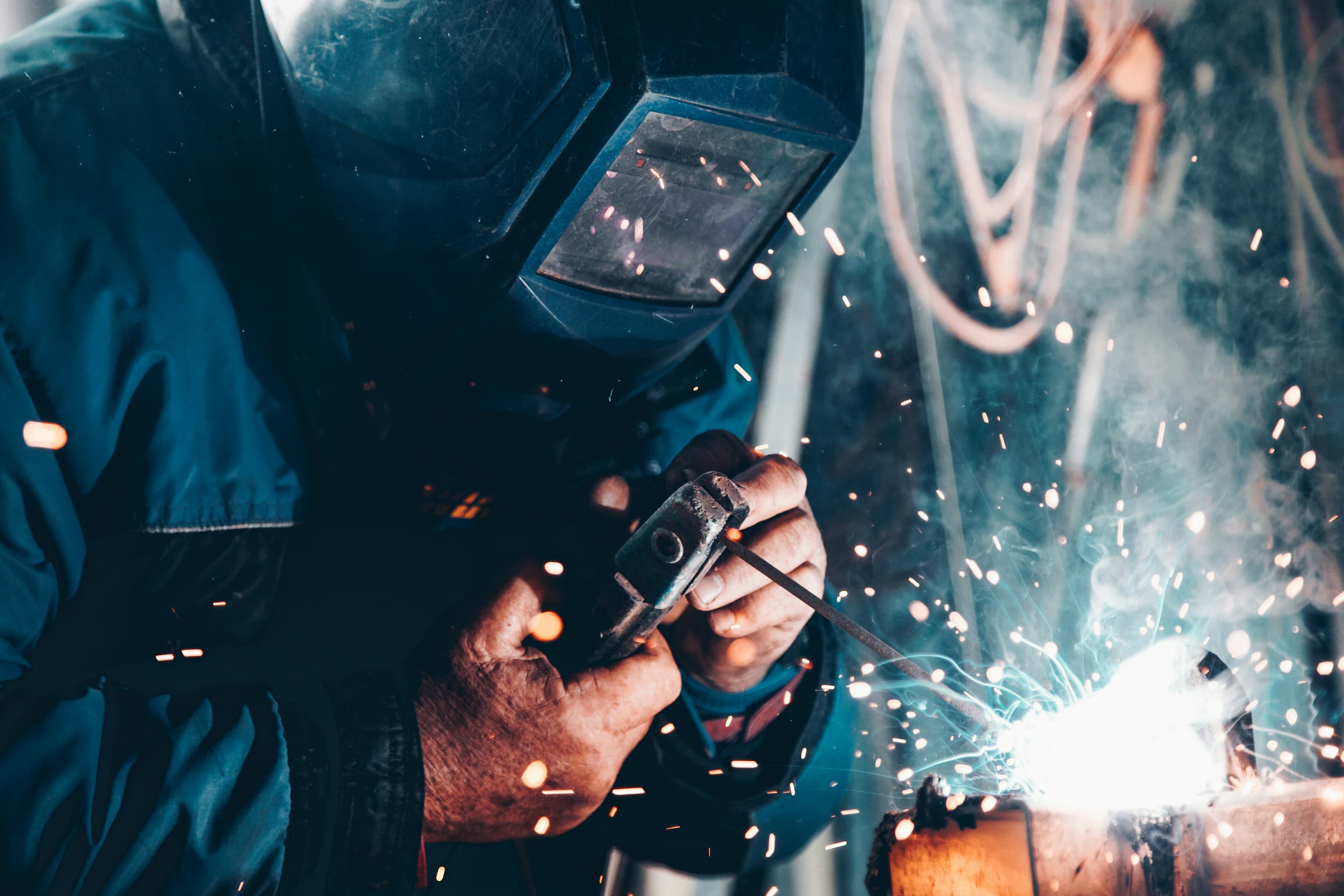 Welder in protective gear using a welding machine, with a bright arc at the work point