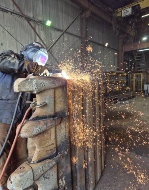 Welder grinding a heavy steel component as sparks fly